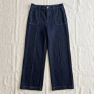 Dark indigo blue wide-leg cropped pants with front pleats and contrast stitching, laid flat on a white fabric background.