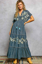 Woman wearing a blue embroidered dress with yellow boots against a gray background