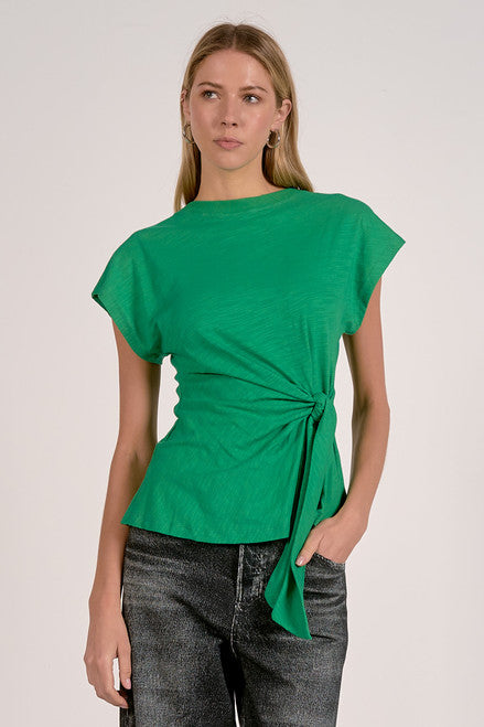 Woman wearing a green top with a tie detail on a plain background