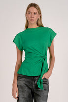 Woman wearing a green top with a tie detail on a plain background