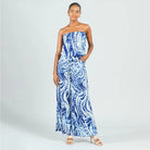A woman modeling a strapless blue and white tie-dye wide-leg jumpsuit against a light gray studio background.
