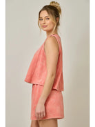 Woman wearing a coral sleeveless top and short set against a plain background