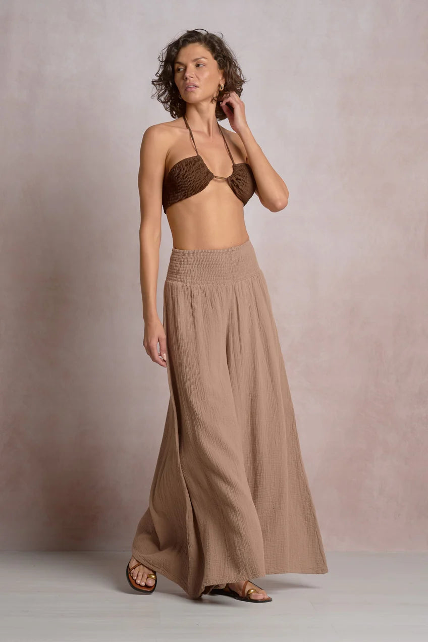 Woman wearing a brown bikini top and long skirt against a plain background