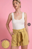 Model wearing White top and yellow shorts against a pink background