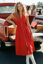 Woman in a red dress standing next to an old red truck with American flags.