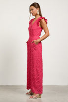 Woman wearing a pink lace dress with ruffled shoulders side view