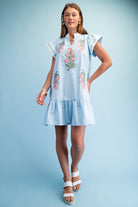 Woman wearing a light blue dress with floral embroidery on a solid background