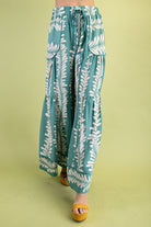 Mint pants with white leaf pattern worn by a person on a green background