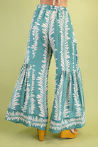 Mint wide-leg pants with white leaf pattern worn by a person on a green background