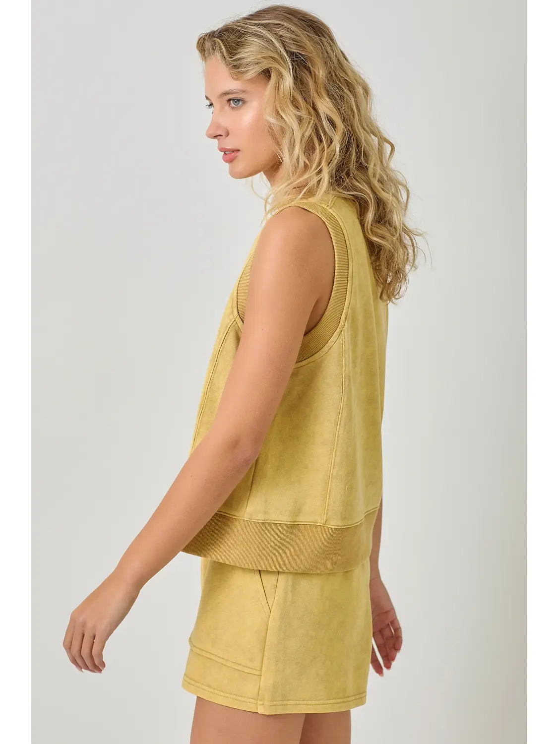 Woman wearing a yellow sleeveless top and shorts set on a white background