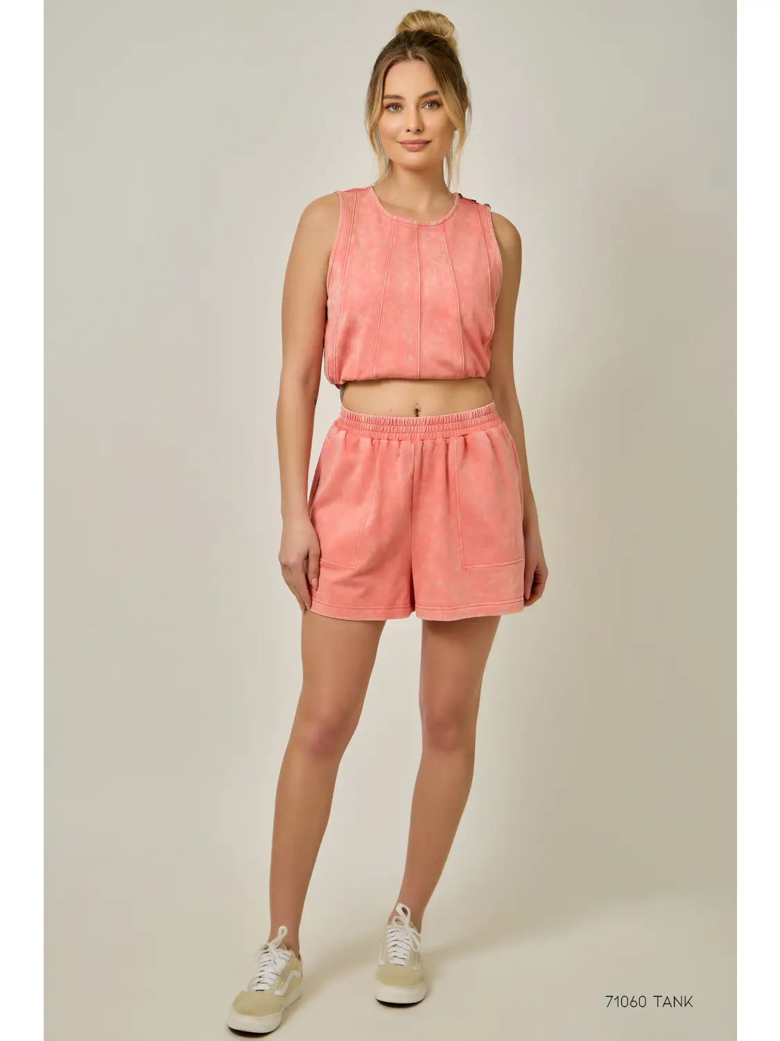 Woman wearing a coral tank top and shorts set on a plain background