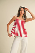 Woman wearing a red and white striped top and white pants against a beige background