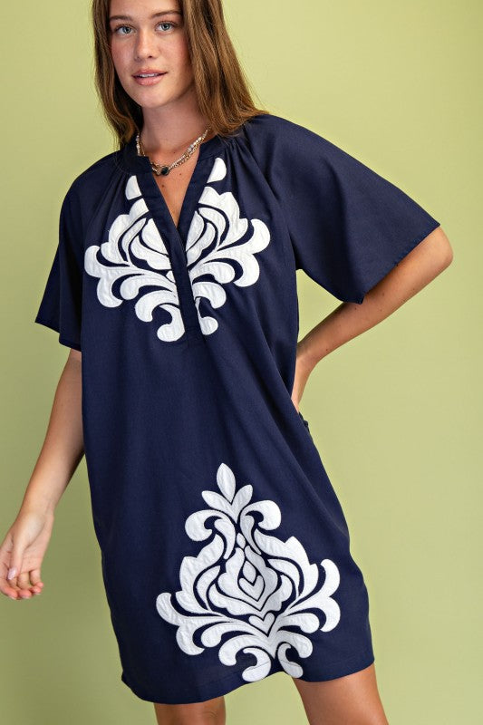 Navy blue dress with white floral patterns worn by a model on a green background