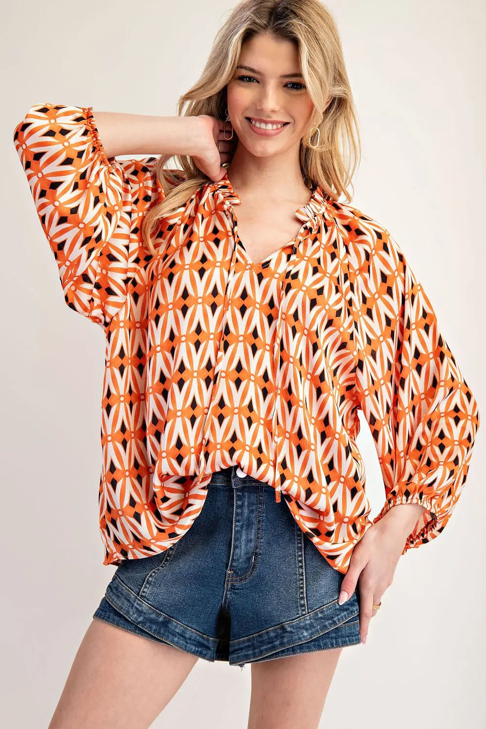 Model wearing orange blouse jean shorts on a white background