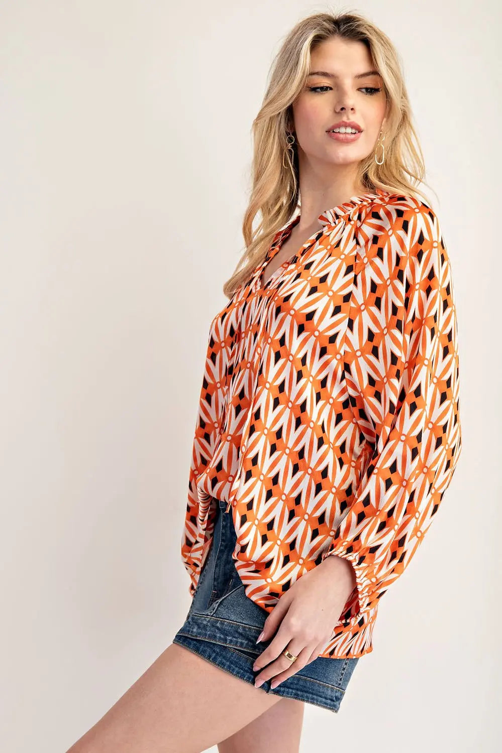 Side view of model wearing orange blouse with jean shorts