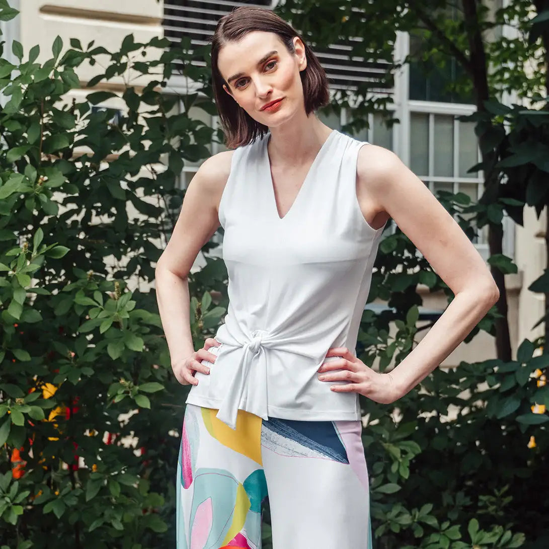 Model wearing white tank top with colorful pants against a bush