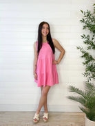 Model wearing tiered, candy, pink, mini dress with neutral wedges against a white wall