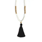 White and gold bead necklace with black tassel on a white background 