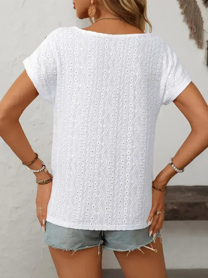 Person wearing a white short-sleeve top with a textured pattern and denim shorts against a neutral background.