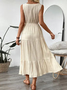 Woman wearing a beige pleated dress in a room with a plant and mirror.