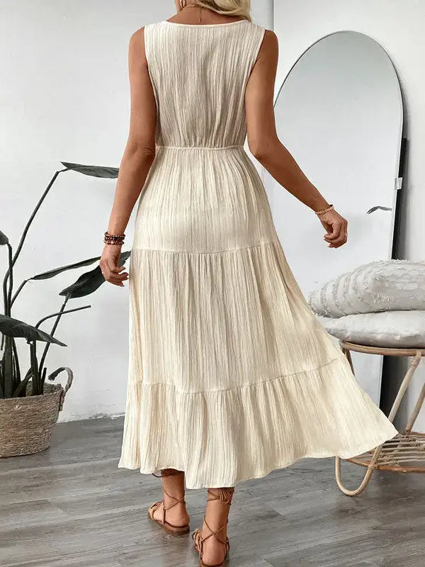 Woman wearing a beige pleated dress in a room with a plant and mirror.