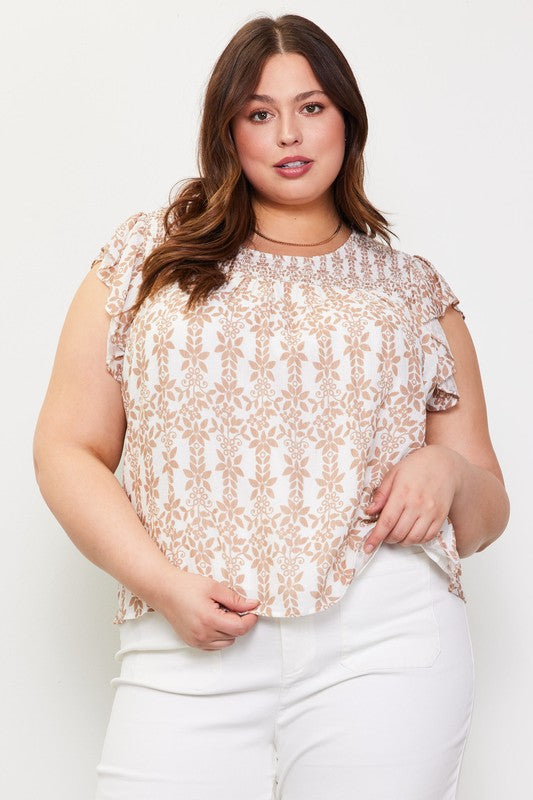 A plus-size woman wearing a short-sleeve top with a beige and white botanical damask pattern, paired with white pants, against a plain white studio background.