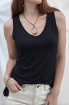 Woman wearing a black tank top and white pants against a plain background