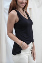 Woman wearing a black sleeveless top and white pants against a plain background