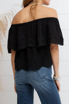 Person wearing a black off-shoulder top and blue jeans against a white background