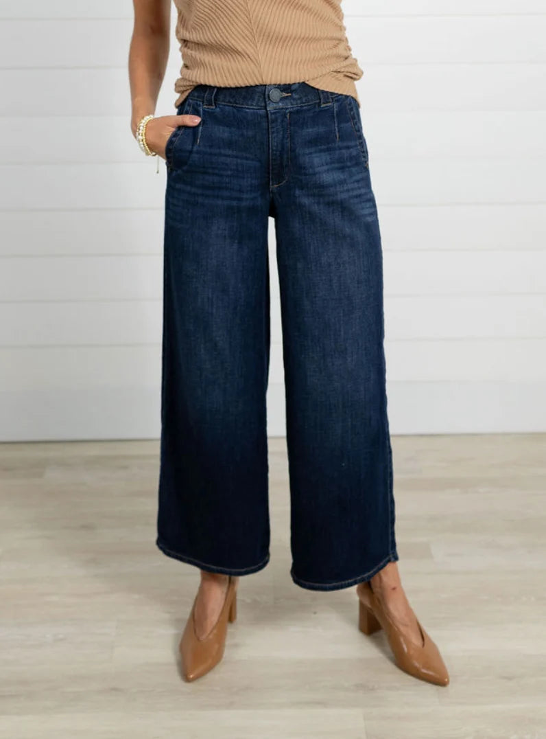 Person wearing blue wide-leg jeans and brown shoes on a light wooden floor.