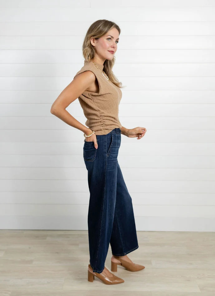 Woman wearing a beige sleeveless top and blue jeans against a white background