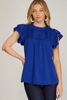 Woman wearing a blue blouse with ruffled sleeves on a plain background