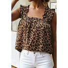 A woman wearing a leopard print ruffled top and white jeans, cropped from the chin down in an indoor setting.