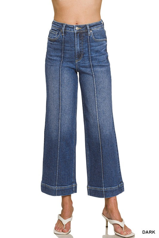 A model wearing a pair of dark blue wide-leg cropped jeans with front seam detailing, shown from the waist down on a white background.