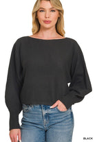 A woman wearing a black wide-neck long-sleeve sweater and blue jeans, shown from the waist up against a plain white background.