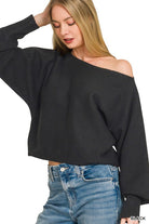 Woman wearing a black off-shoulder sweater and blue jeans on a white background