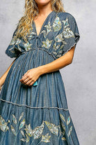 Woman wearing a blue denim dress with floral embroidery on a gray background