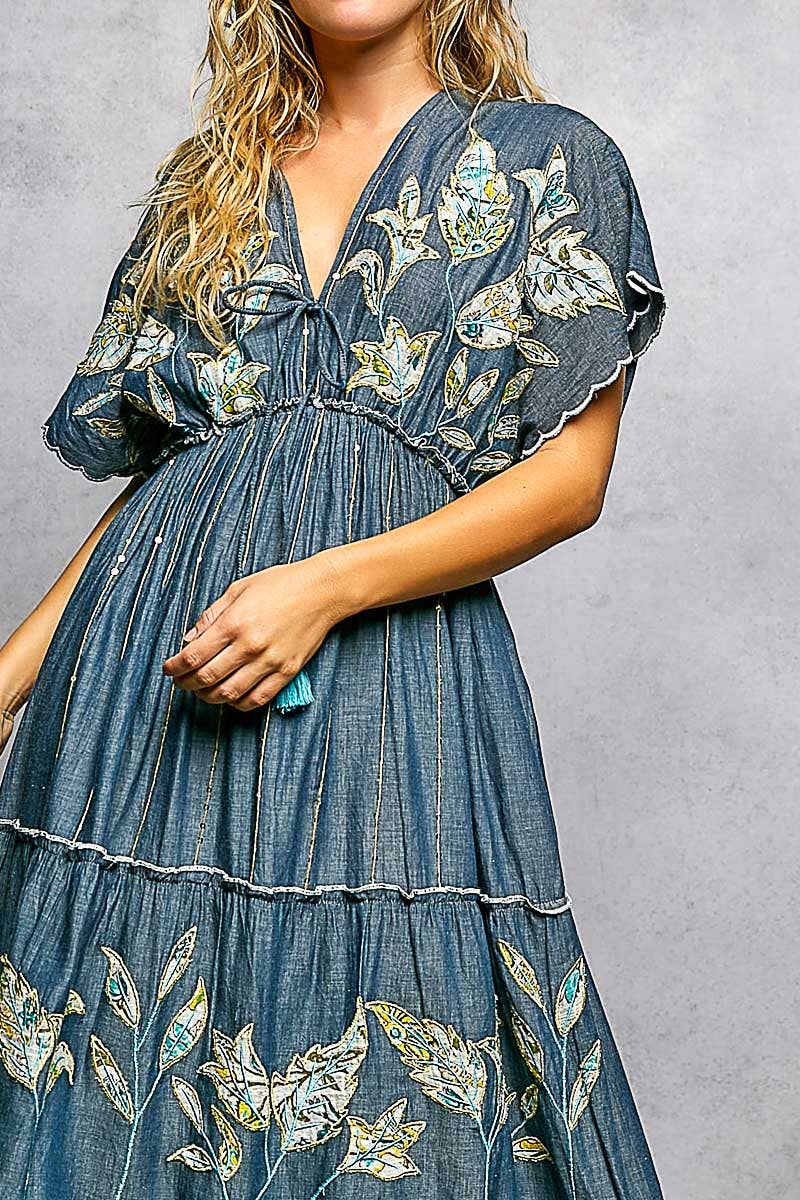 Woman wearing a blue denim dress with floral embroidery on a gray background