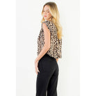 A woman wearing a sleeveless leopard-print top and black pants, photographed from the back against a plain white studio background.