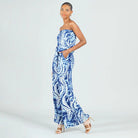 A woman modeling a strapless blue and white patterned maxi dress with a tie-dye style design, standing against a light gray studio background.