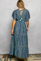 Woman wearing a blue denim dress with tassel details on a plain background