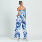 A woman shown from the back wearing a strapless wide-leg jumpsuit with a blue and white tie-dye swirl pattern, paired with beige high heels, against a light gray studio background.