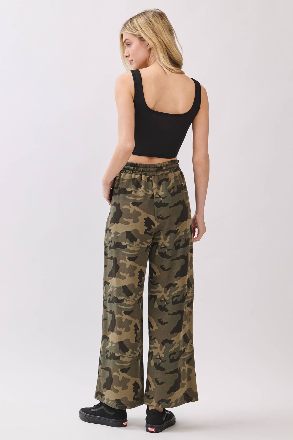 Woman wearing camouflage pants and a black top on a white background