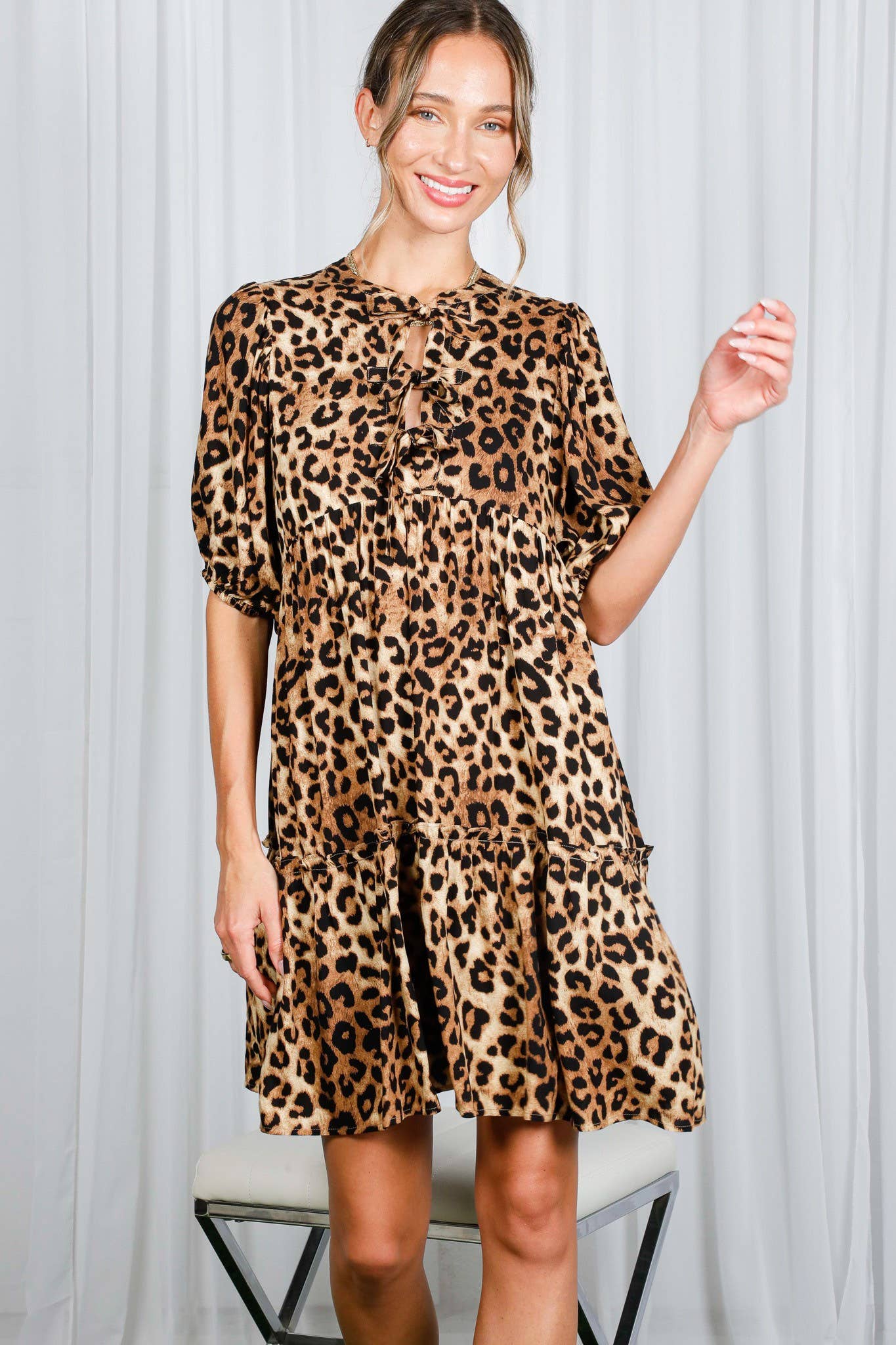 Woman wearing a leopard print dress against a white curtain background