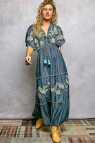 Woman wearing a blue floral dress with tassels against a gray background